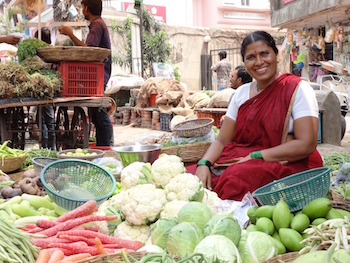 A woman selling fruits and vegetables at an outdoor market in India.