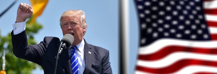 Donald Trump giving a speech with a raised fist in front of an American flag