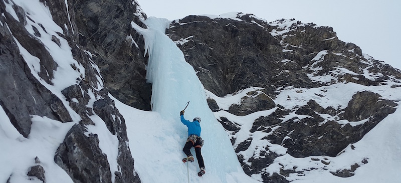 A mountain climber with an ice pick in hand climbing an icy mountainside