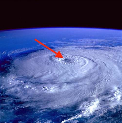 An aerial view of a hurricane with a red arrow pointing to the eye of the storm