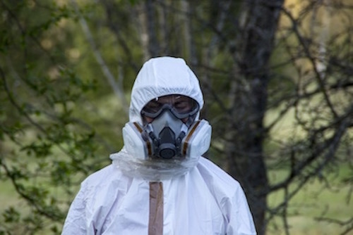 A person wearing a white hazmat suit with trees in the background