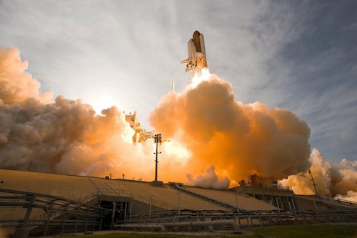 A space shuttle takes off with billows of exhaust smoke below